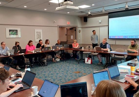 A room full of people with laptops listening to a speaker